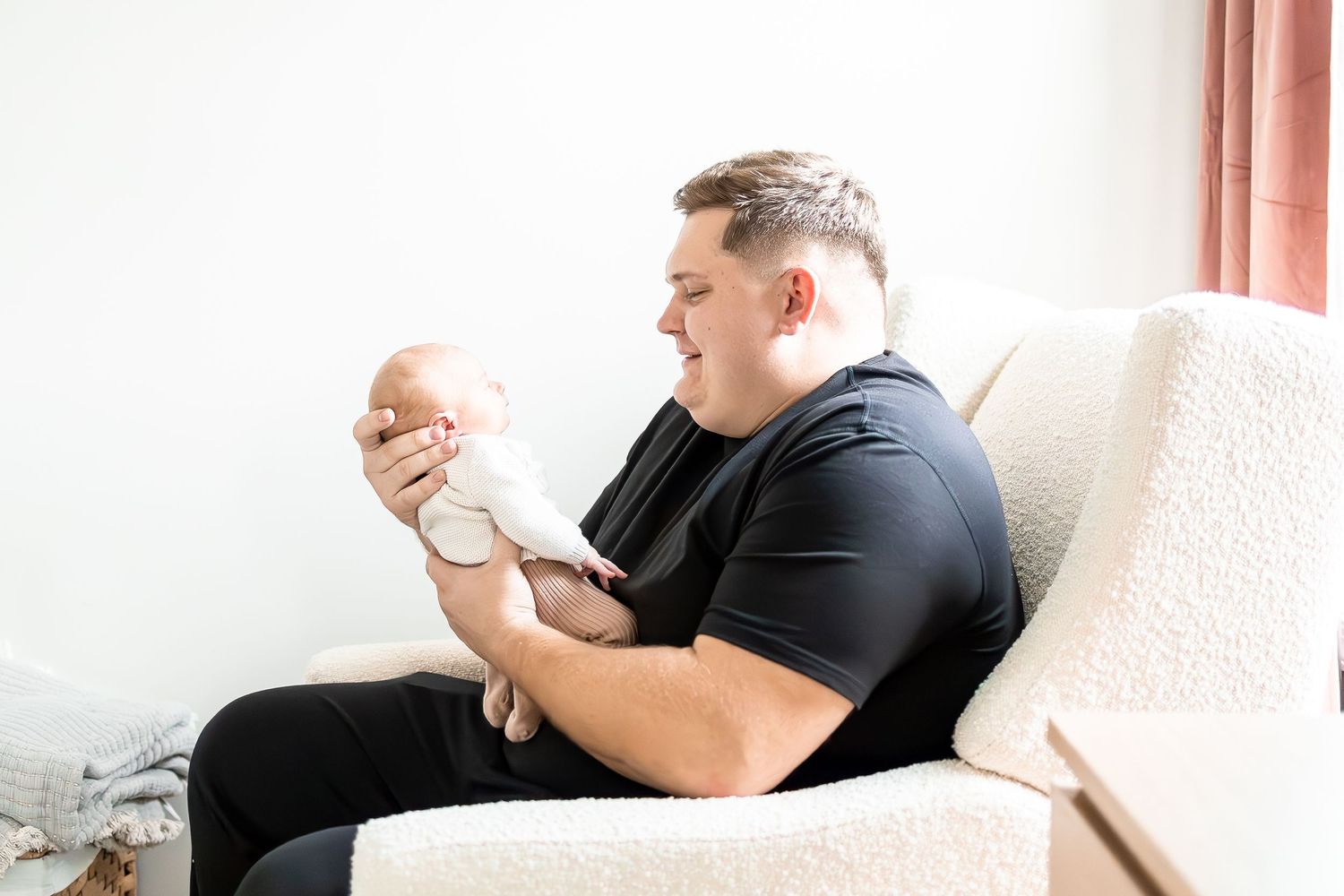 A person in black clothing cradles a sleeping newborn baby while sitting on a white couch.