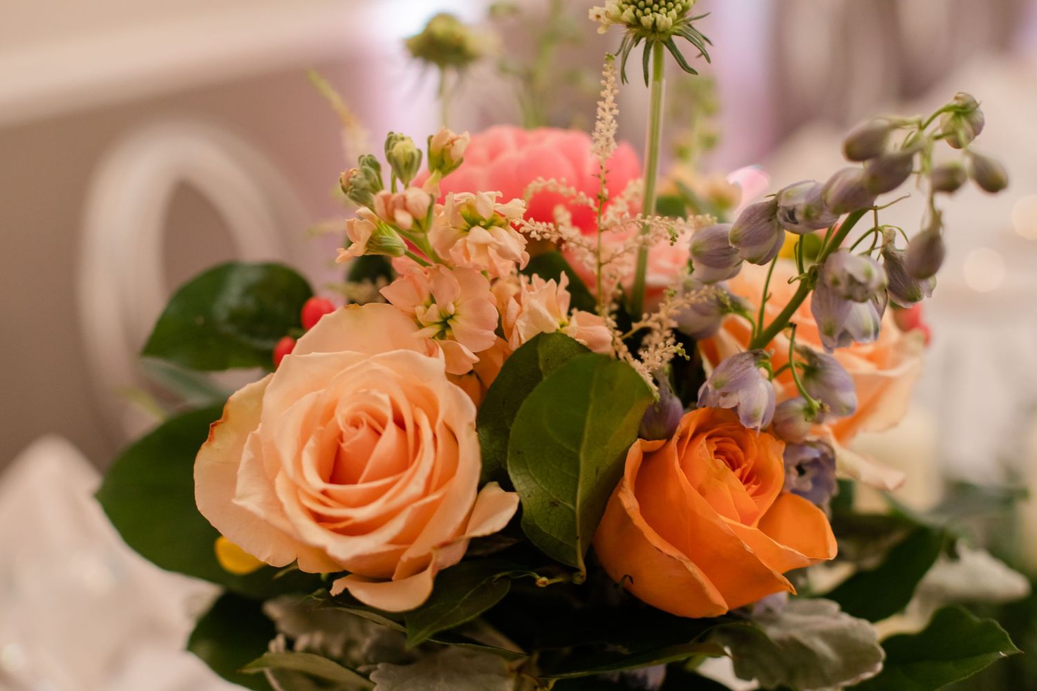 Peach and coral roses arranged with greenery in an elegant wedding centerpiece.