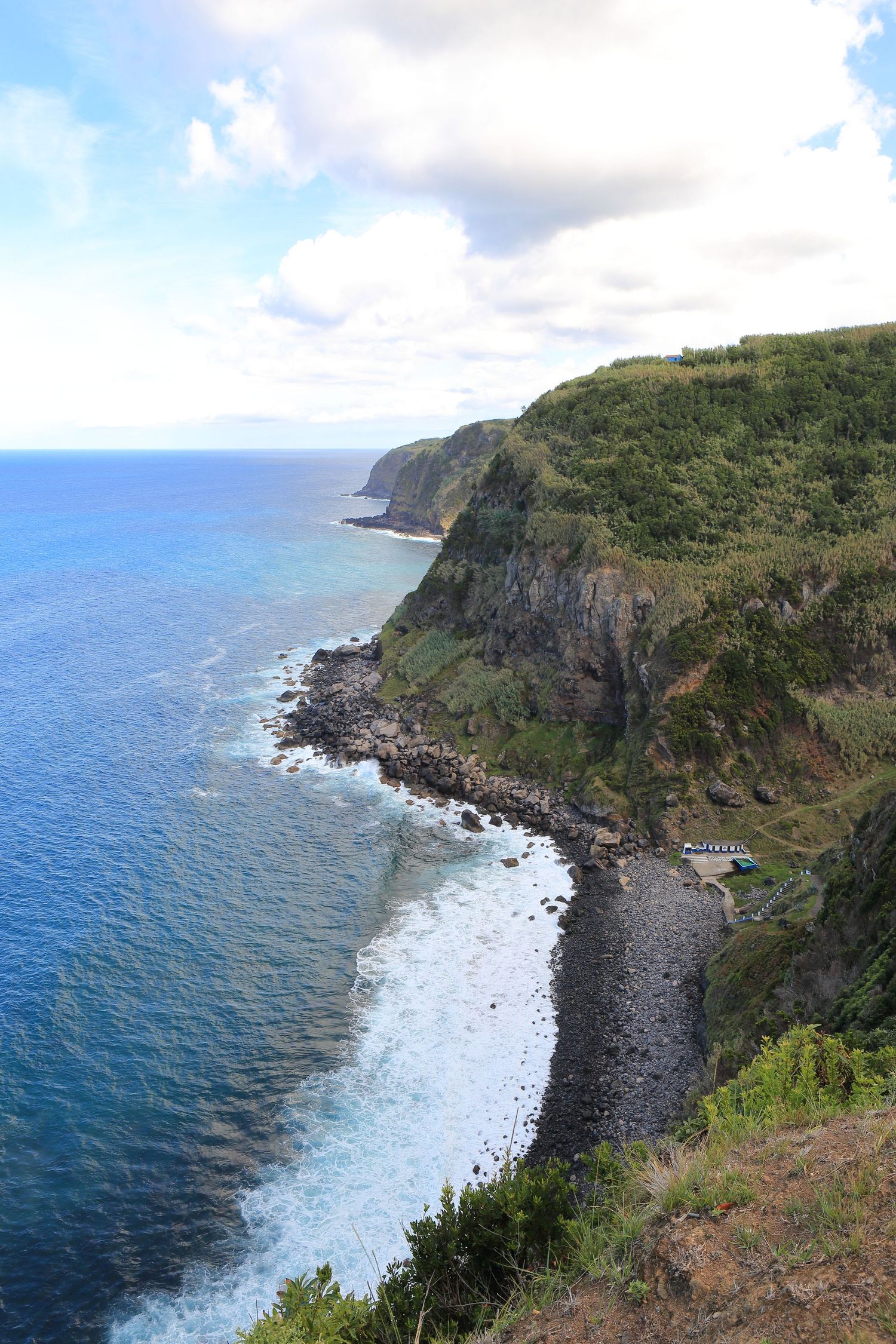 Dramatic coastal cliffs rise above a rocky beach where waves crash against the shoreline.