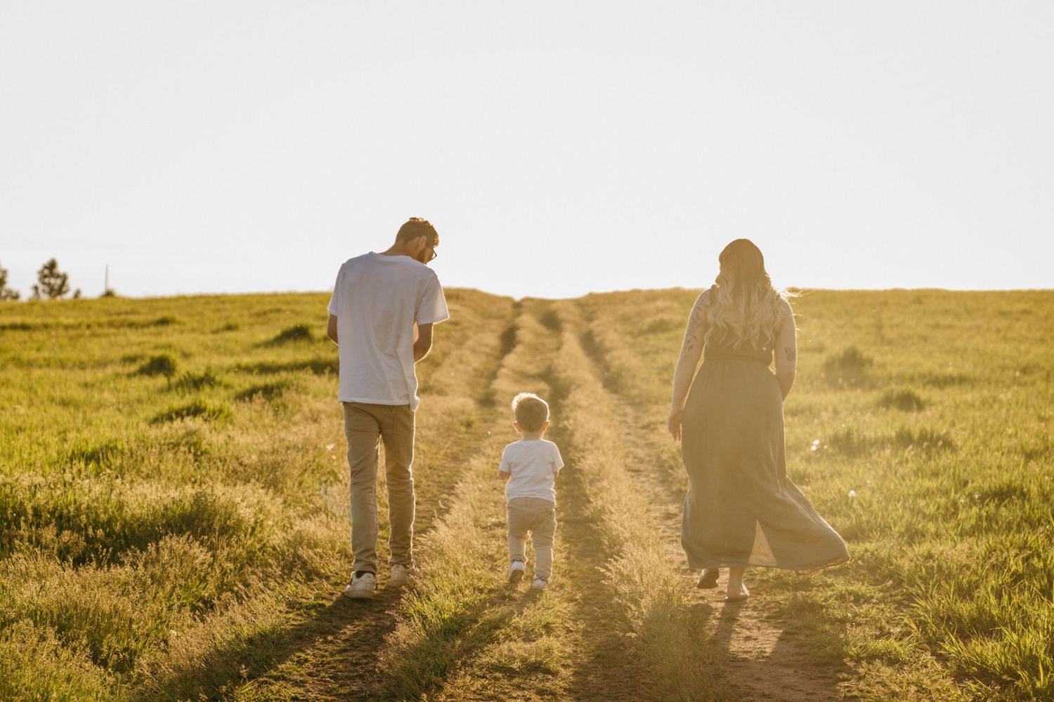 Silhouettes walking together on a dirt path through a sunlit meadow at golden hour.