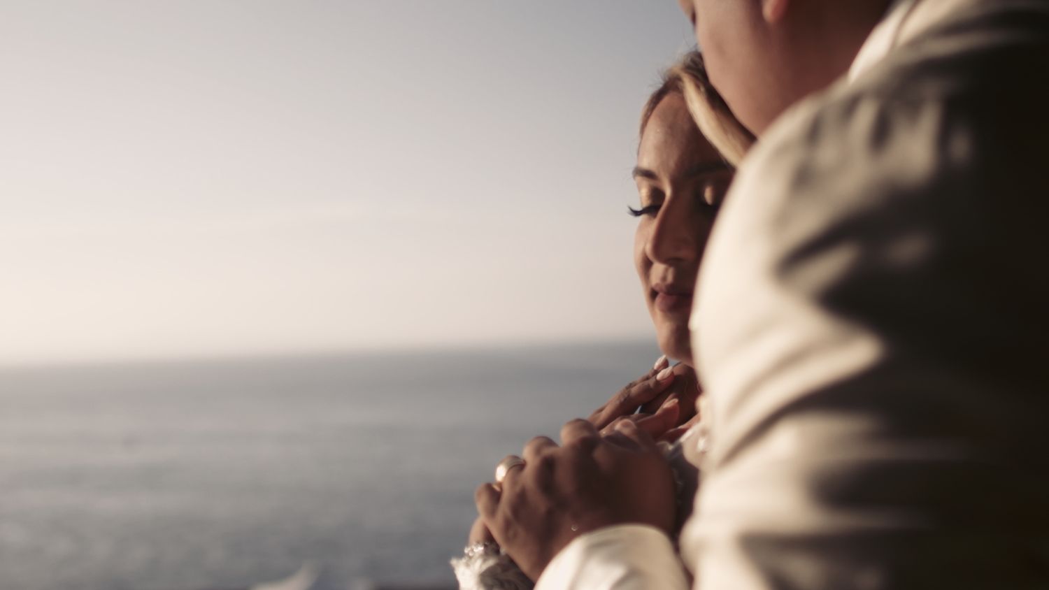 Intimate close-up of a couple's hands during a seaside wedding moment.
