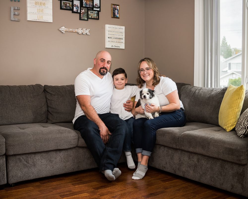 A family snuggles together with their dog at home on their couch.