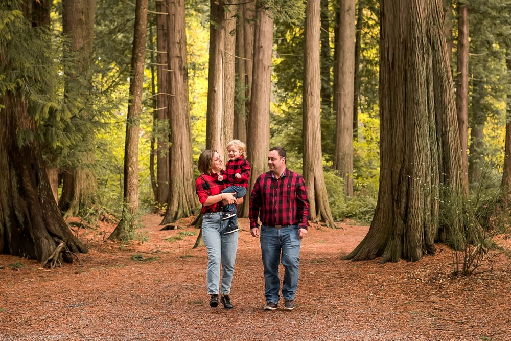 A family of three go for an autumn walk together along a forest path lined with trees. Pitt Meadows, BC.