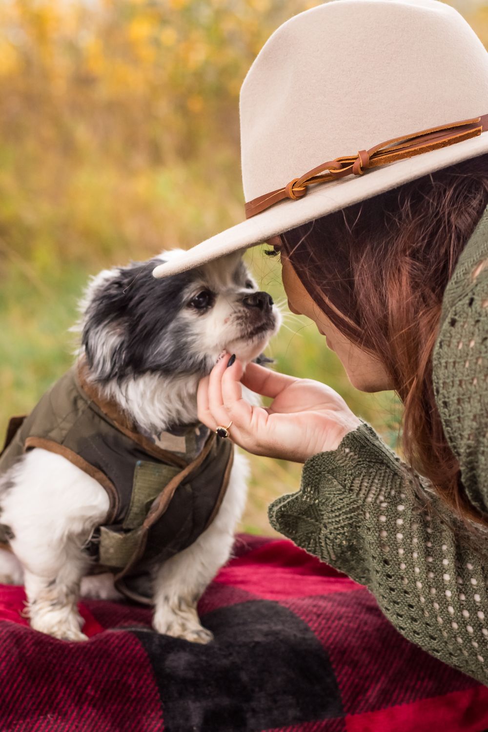 A woman stylishly dressed and wearing a hat leans down to look in to her dog's eyes.