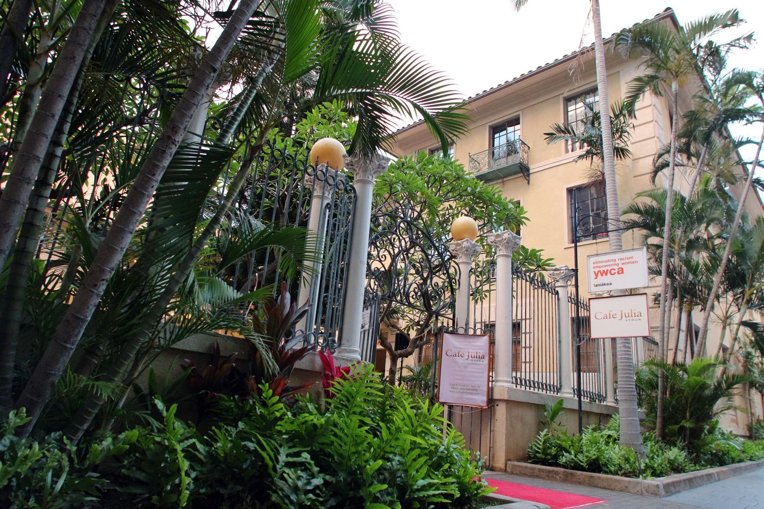 Lush tropical entrance of an elegant Hawaiian hotel surrounded by palm trees and colorful gardens.