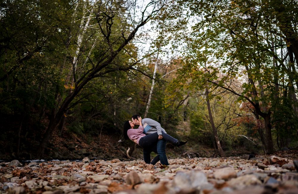 Wide panoramic view of a wooded park path covered in fallen autumn leaves.