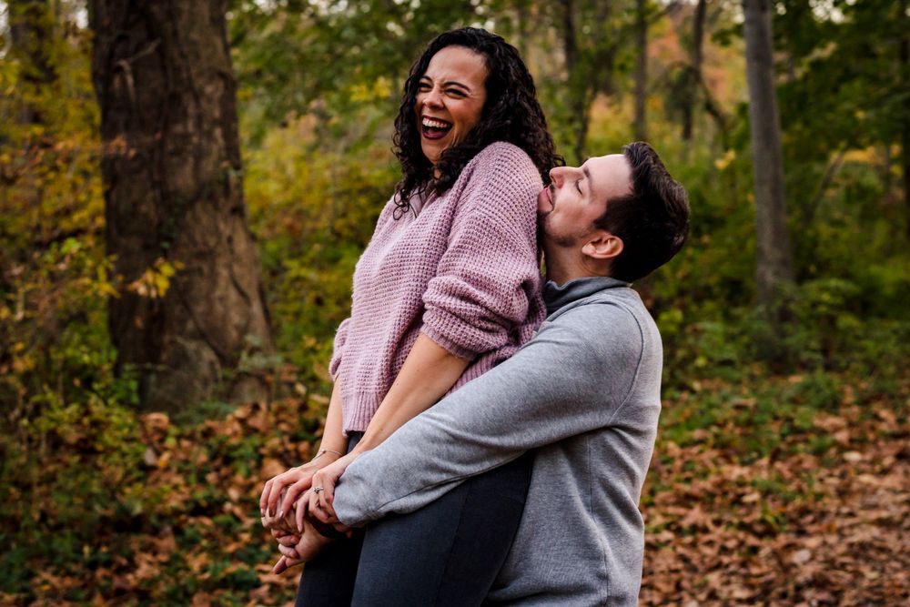 Couple laughing together in a forest setting with autumn foliage in the background.
