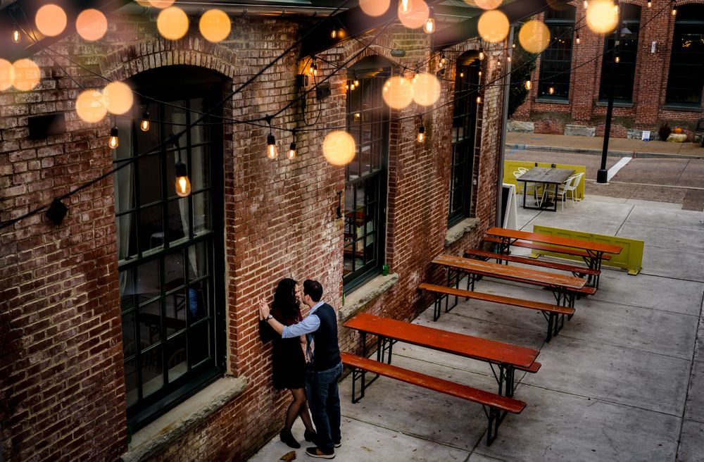 String lights illuminate a brick courtyard with wooden benches creating a warm ambiance.