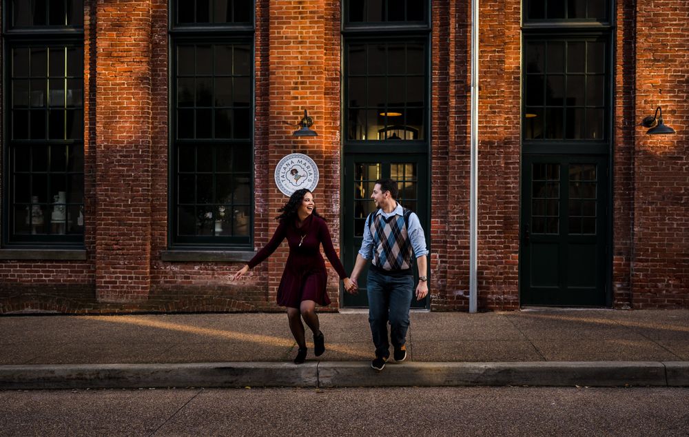 A couple walks along a brick building exterior with dramatic evening lighting.