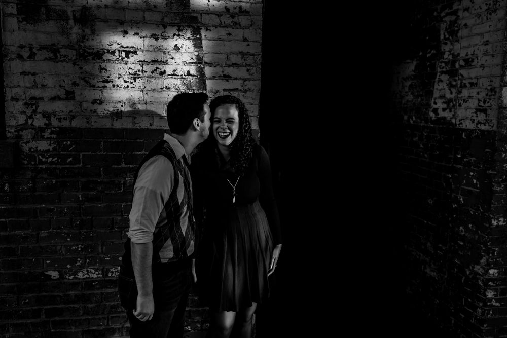 Intimate black and white portrait of a couple against textured brick walls.