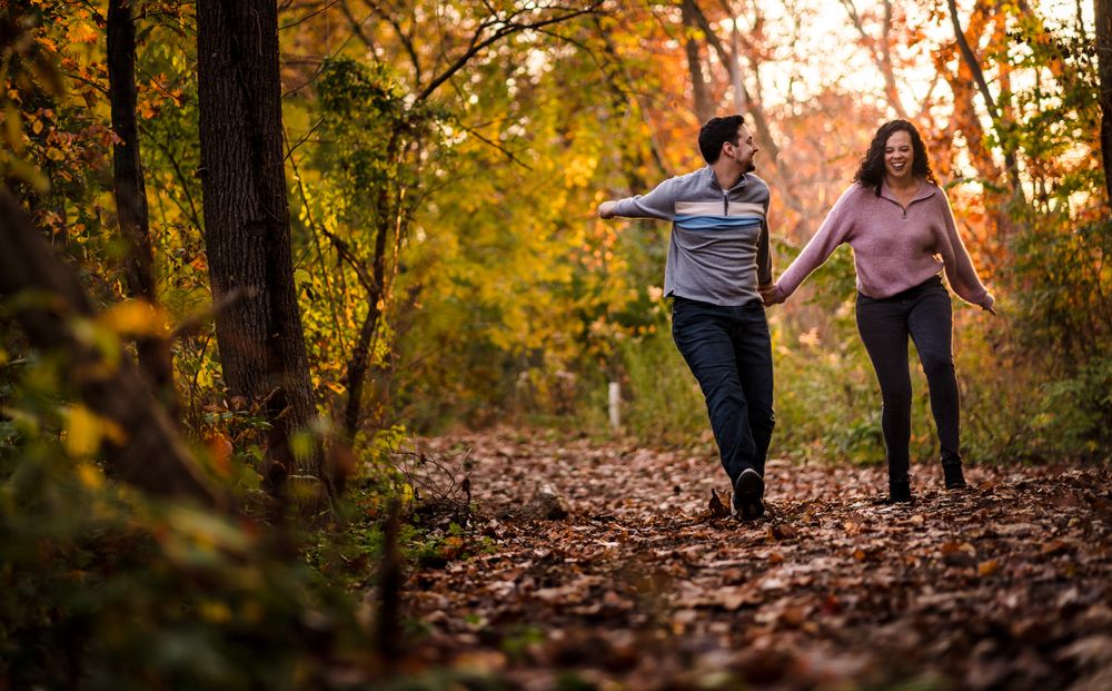 Couple walking through autumn leaves in a forest with golden sunlight streaming through trees.