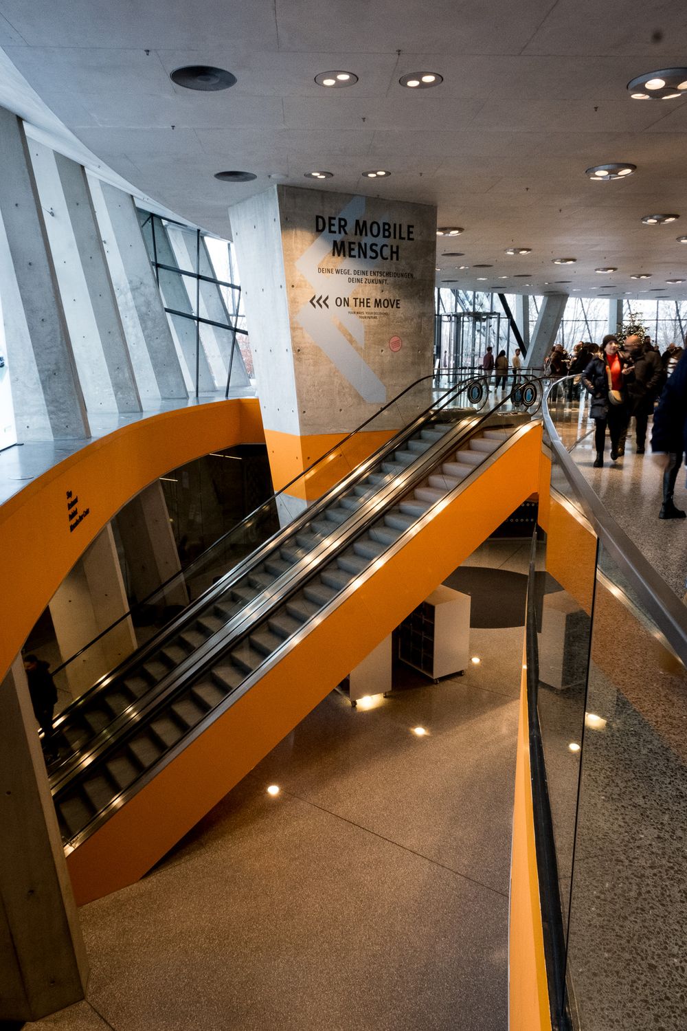Interior escalators and orange ramps inside the Mercedes-Benz Museum with Der Mobile Mensch exhibit sign.
