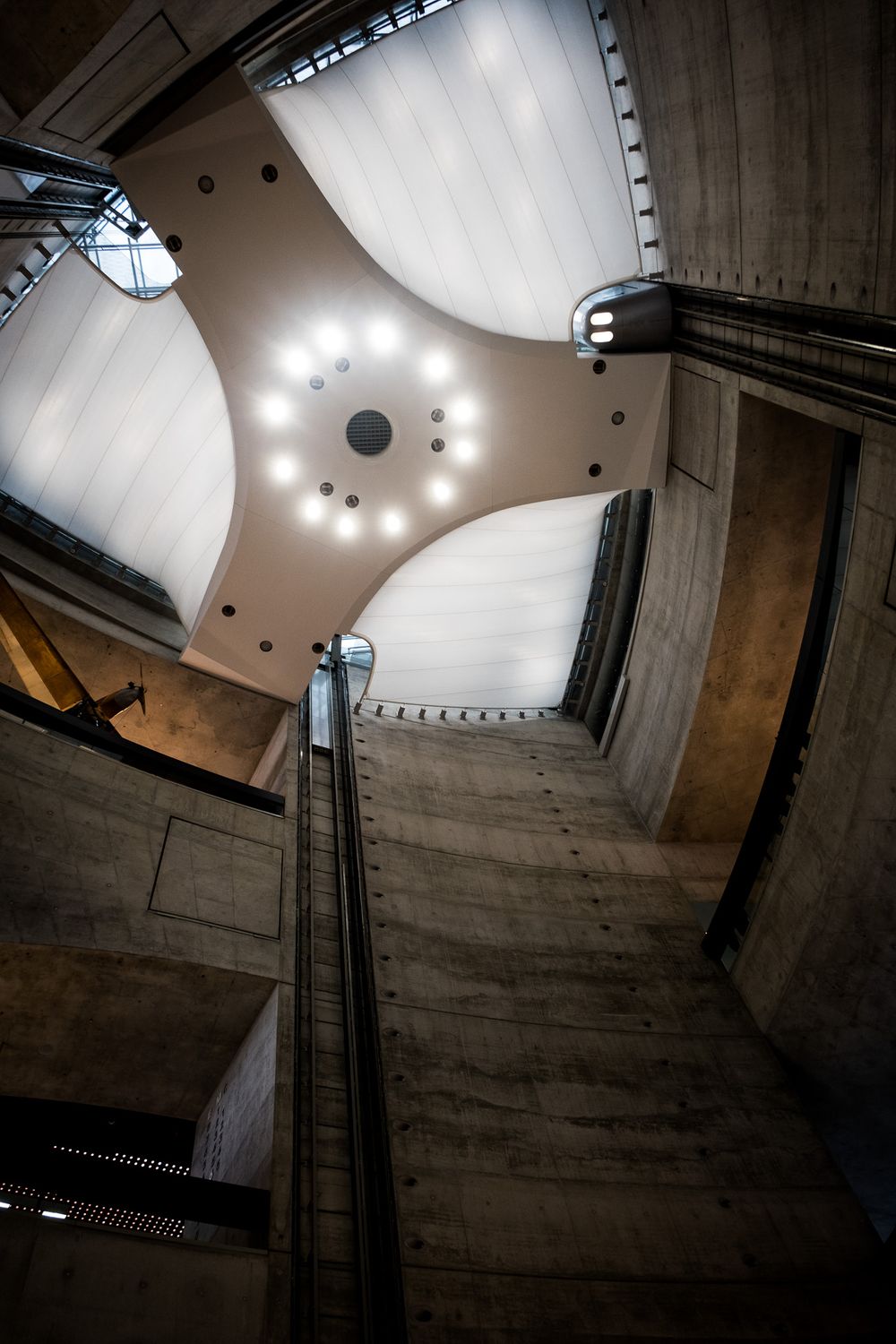 Looking up at the domed ceiling of the Mercedes-Benz Museum in Stuttgart, featuring curved concrete architecture and circular lighting.