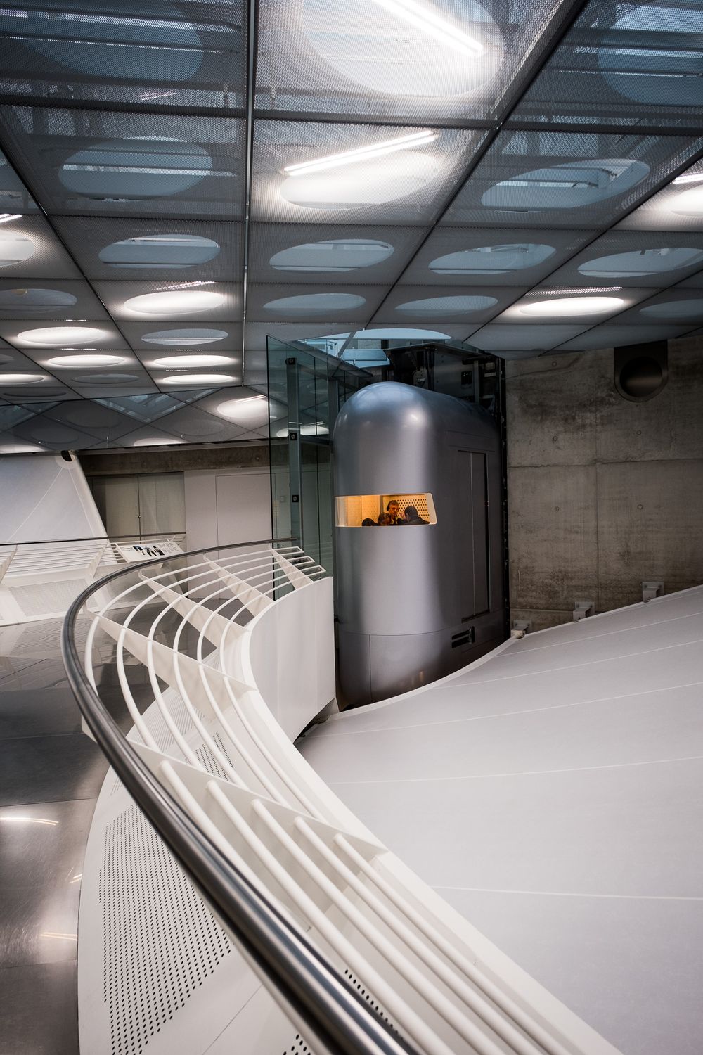 Modern interior of the Mercedes-Benz Museum featuring curved white ramps, glass ceiling panels, and a cylindrical elevator shaft.