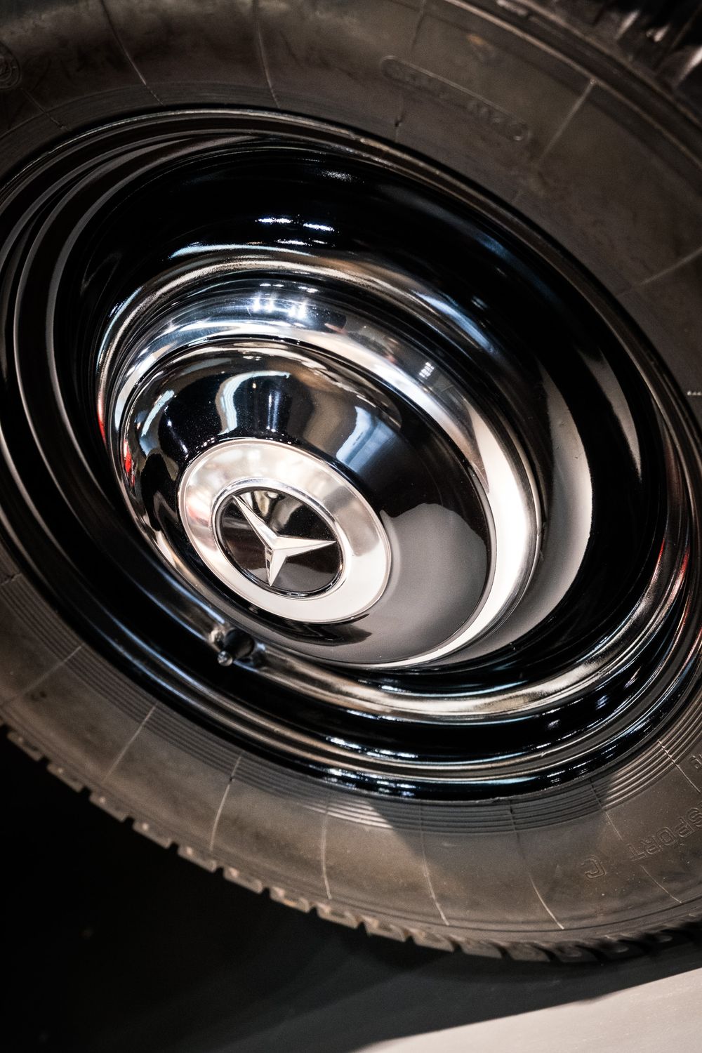 Close-up of a shiny chrome Mercedes-Benz hubcap with three-pointed star logo on a classic black wheel.