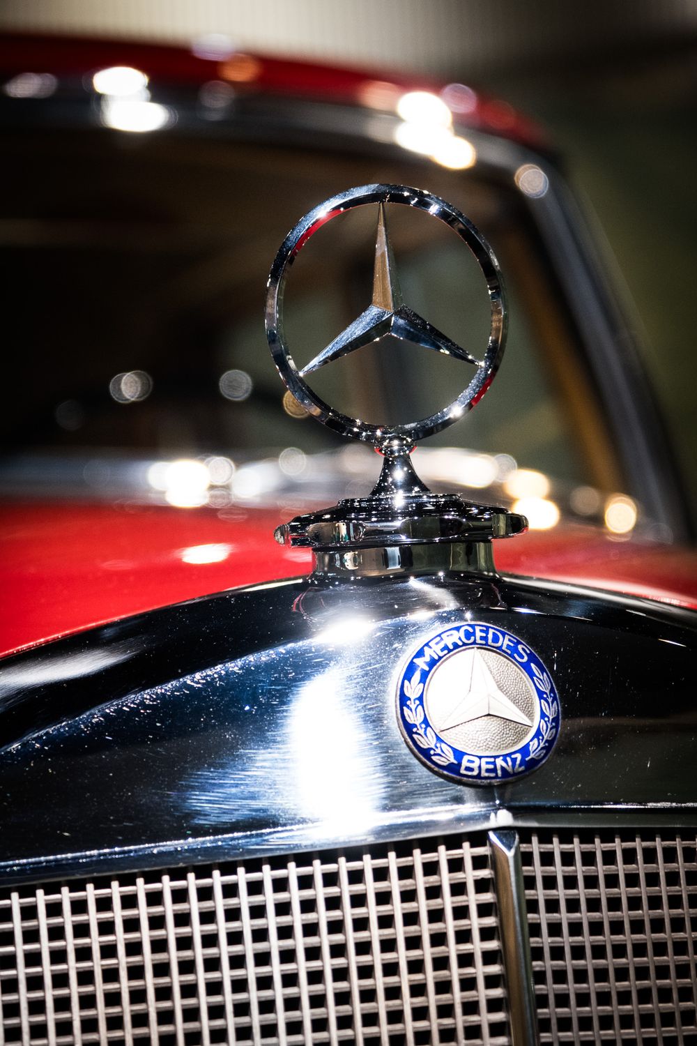 Gleaming chrome Mercedes-Benz three-pointed star hood ornament and blue enamel badge on a classic black car.