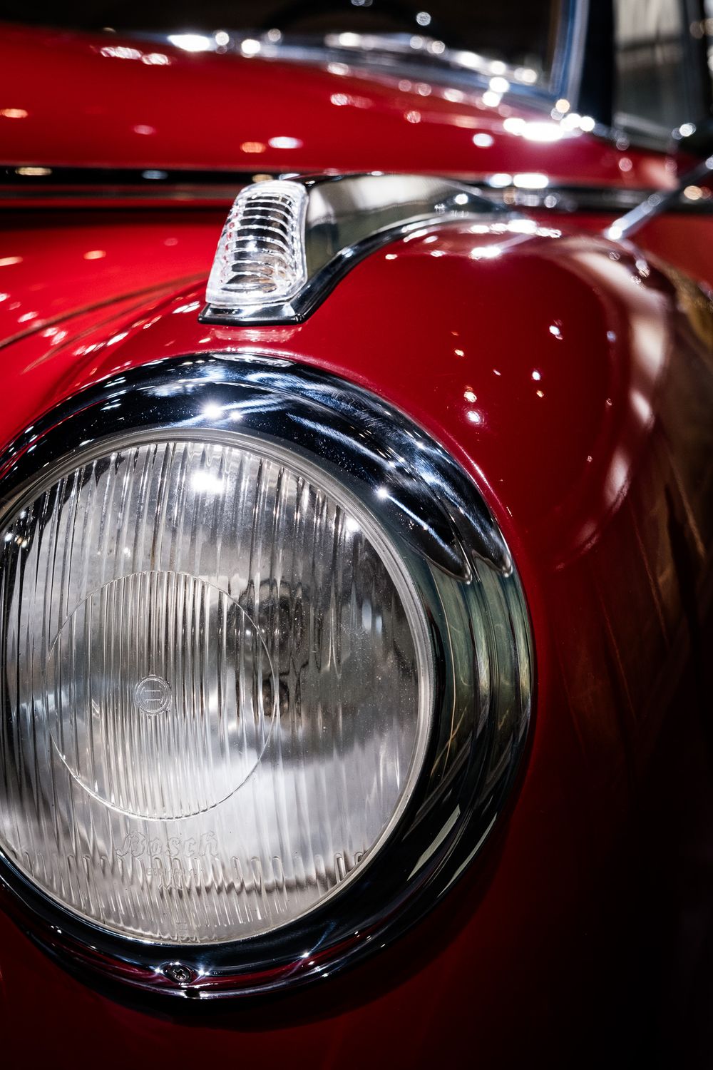 Close-up detail of a round chrome headlight on a beautifully restored vintage red Mercedes-Benz classic car.