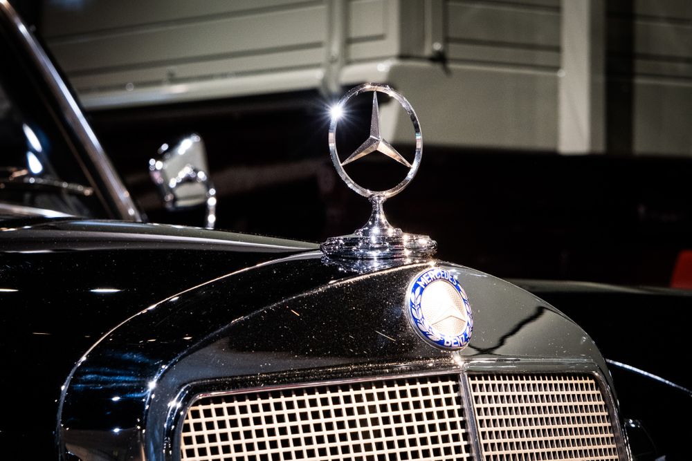 Polished chrome Mercedes-Benz three-pointed star hood ornament gleaming on a classic black vintage luxury automobile.
