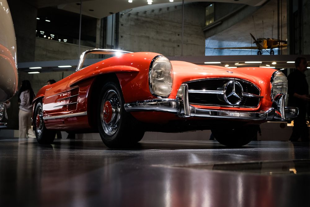 Iconic red Mercedes-Benz 300SL Roadster classic sports car on display in a modern museum exhibition hall.