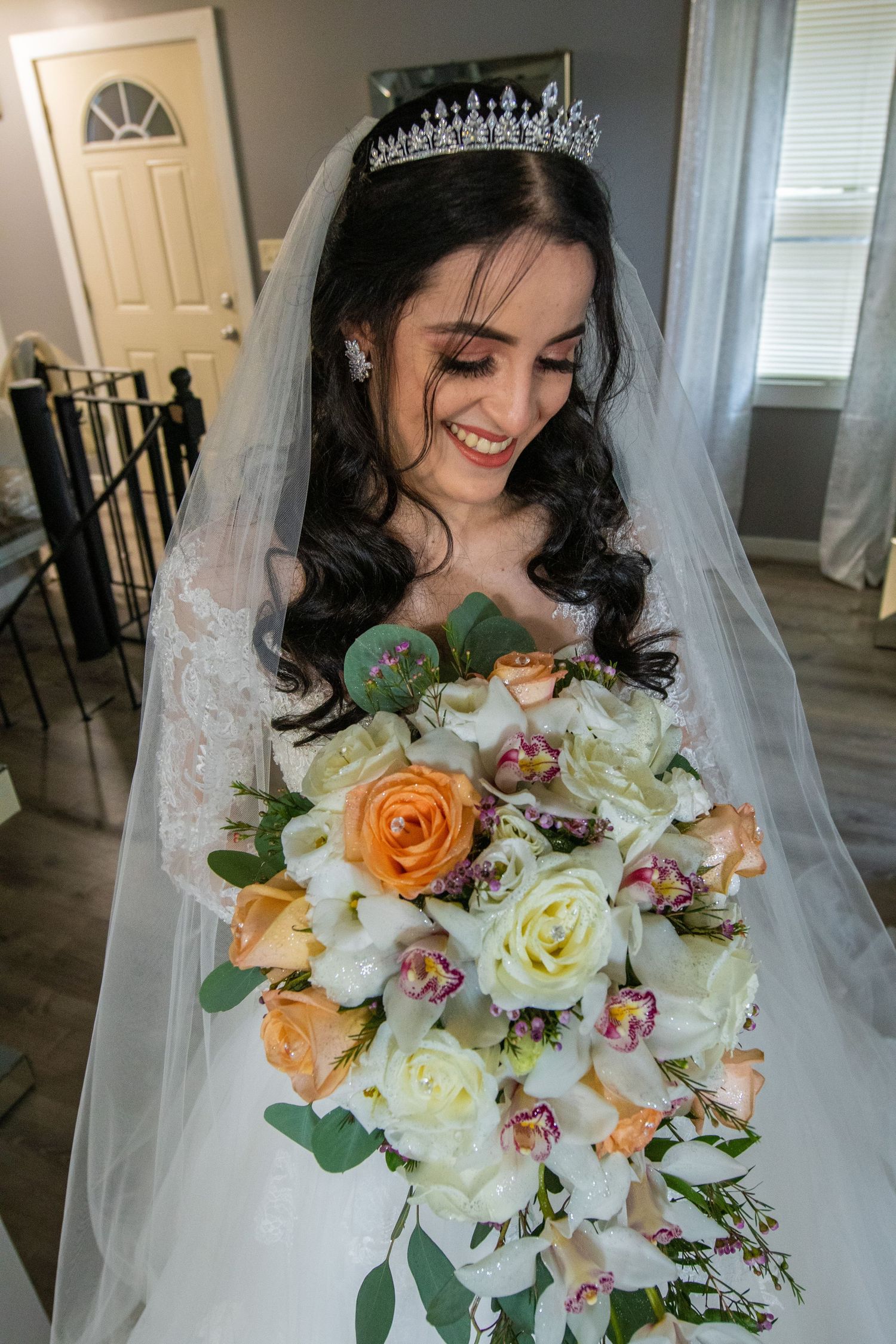 Beautiful bridal bouquet with orange roses, white orchids and mixed florals against a light indoor background.