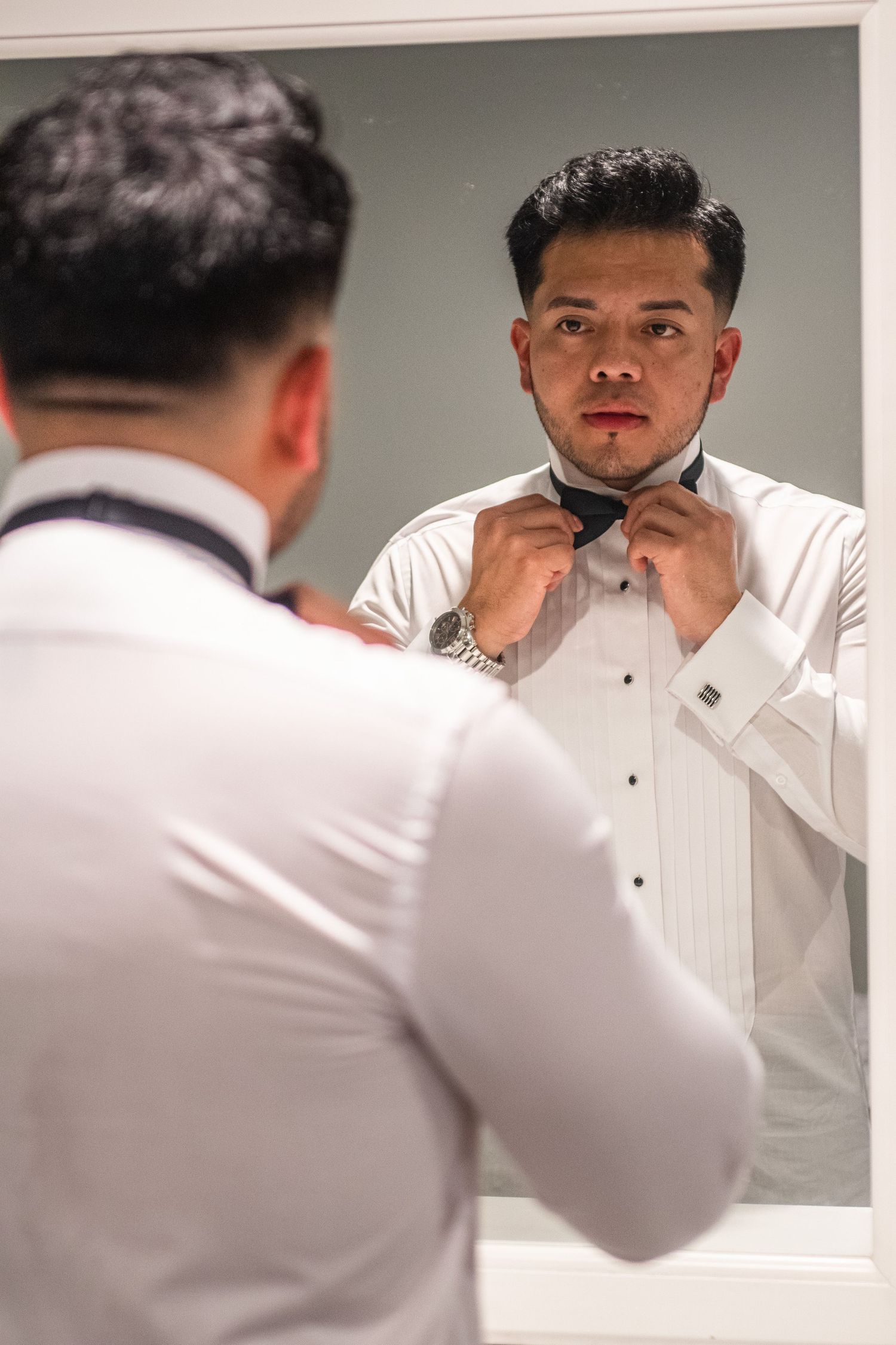 Groom checking his appearance and adjusting his tie in a bathroom mirror.
