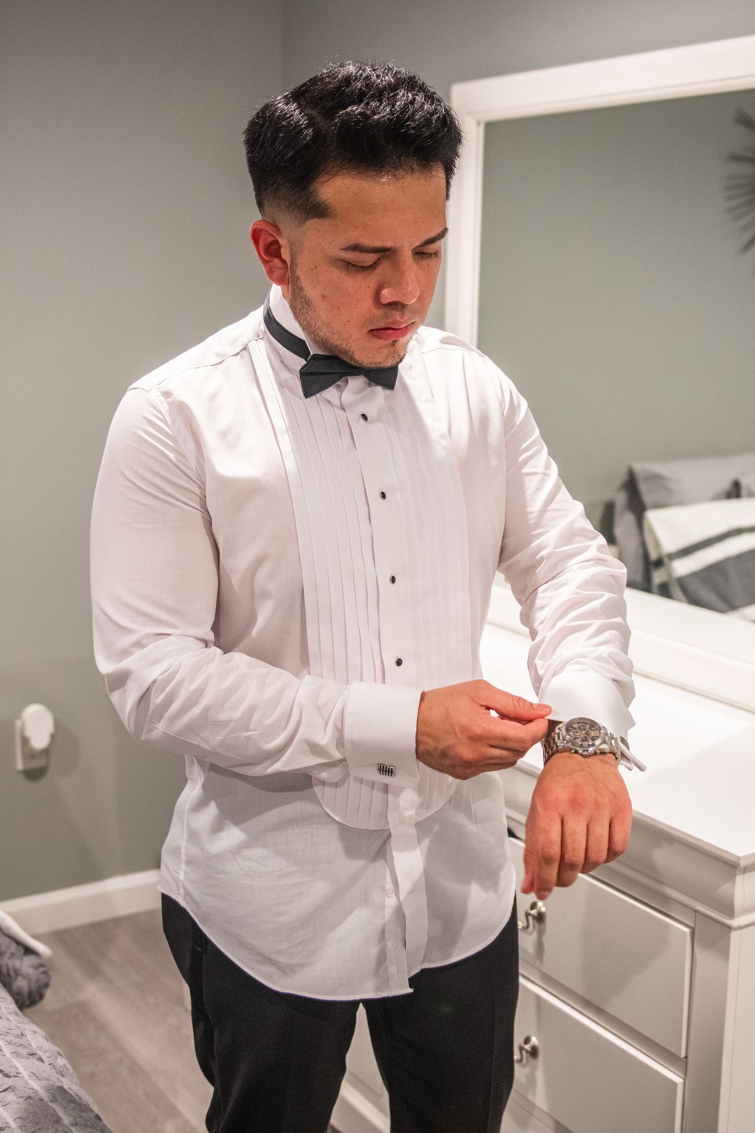 Groom adjusting his white tuxedo shirt and cufflinks while getting ready.