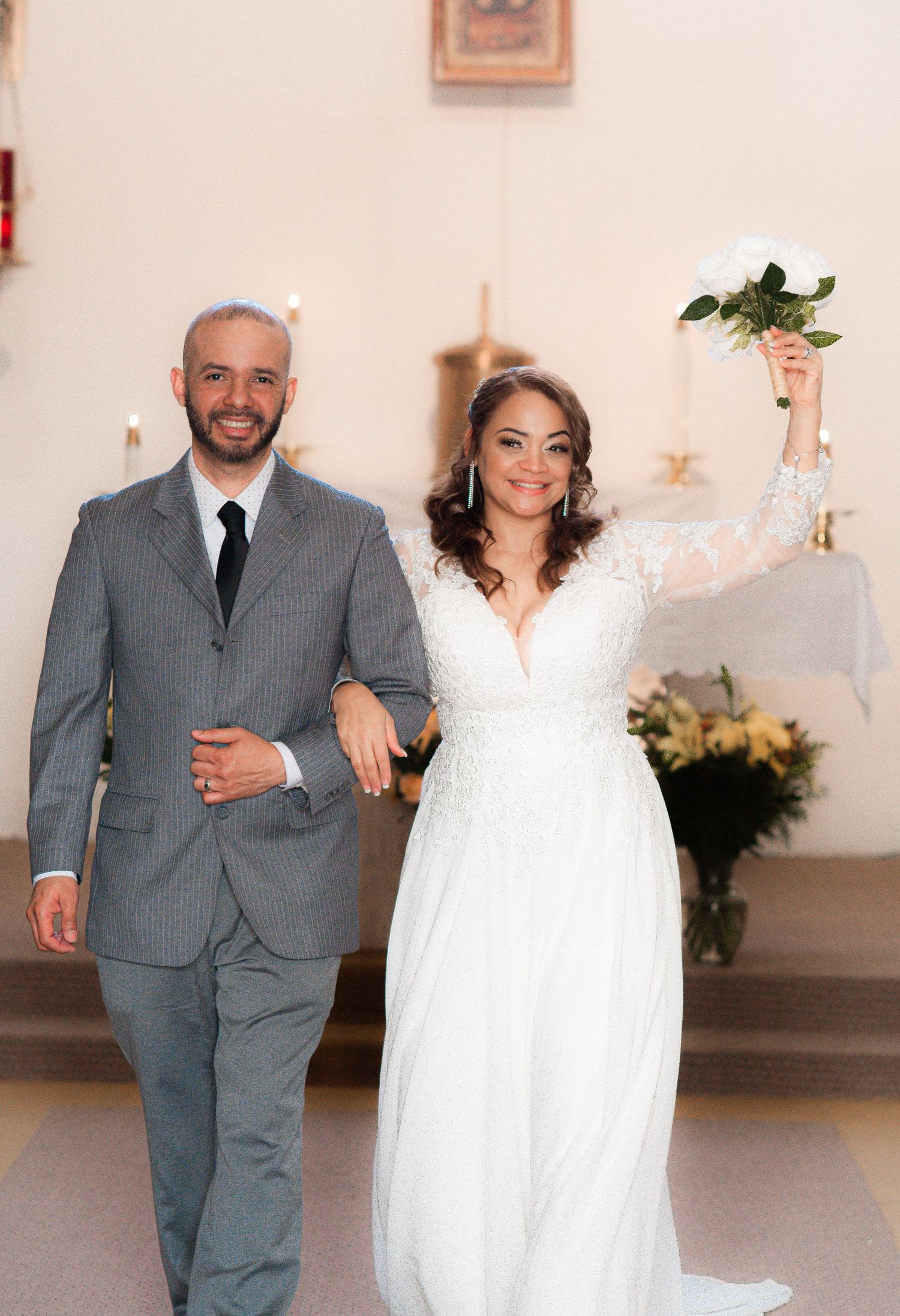 Wedding couple walking down church aisle in white dress and gray pinstripe suit.