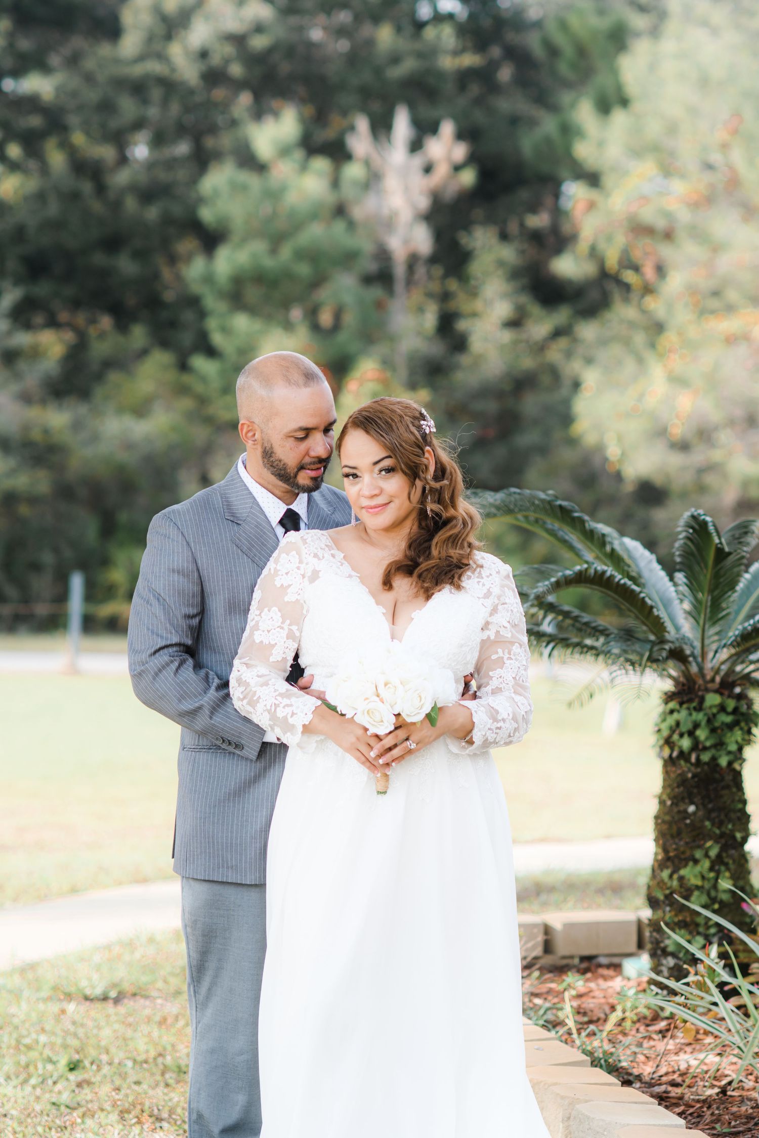 Romantic outdoor wedding portraits with couple in white dress and gray suit among garden greenery.