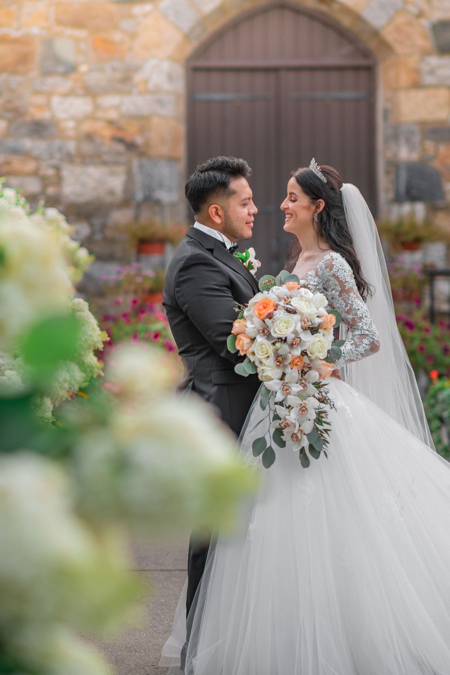 A romantic wedding portrait in front of a stone church with a beautiful floral bouquet.