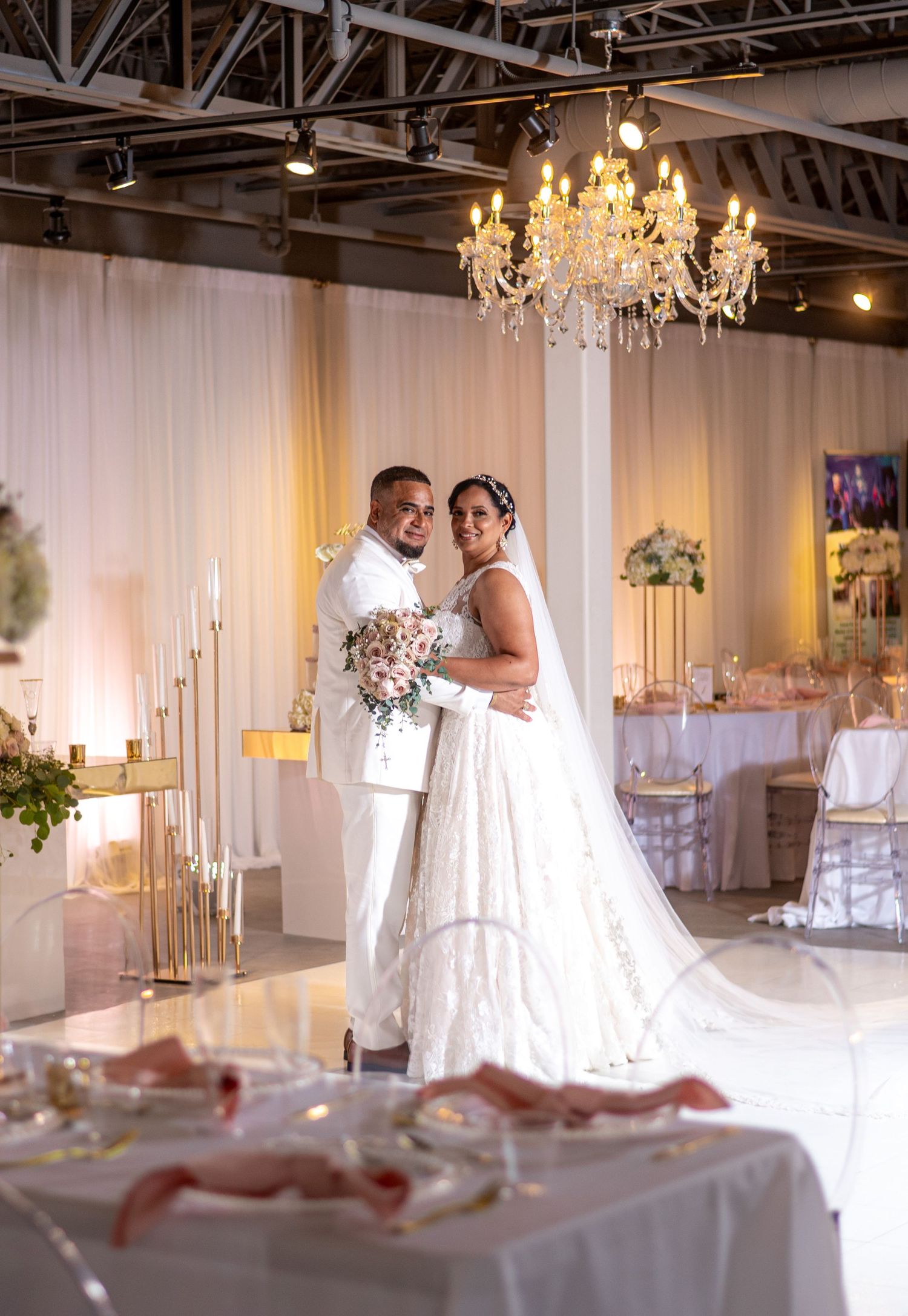 A wedding reception venue decorated with white draping, chandeliers and elegant table settings.