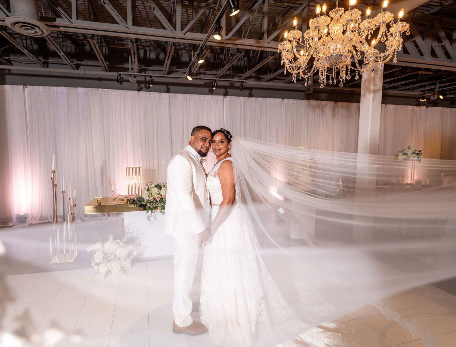 A spacious wedding venue featuring white draping, chandeliers and romantic lighting.