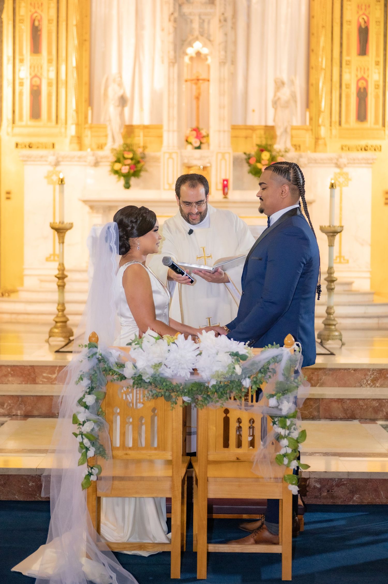 Wedding ceremony in ornate church with golden altar and decorative floral arrangements.