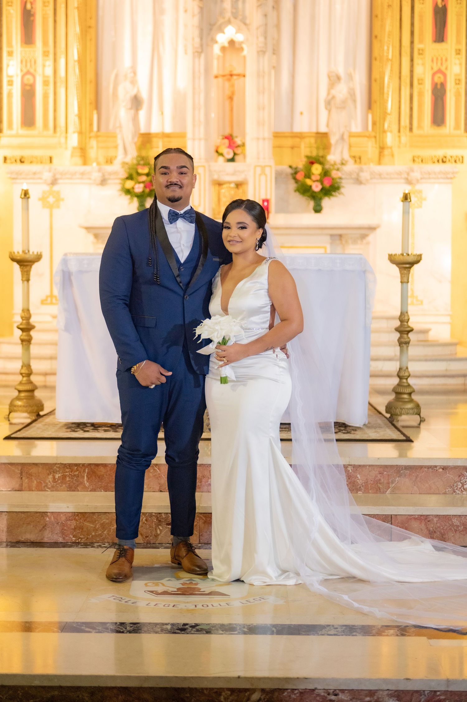 Elegant church wedding ceremony with couple seated before golden altar and floral decorations.