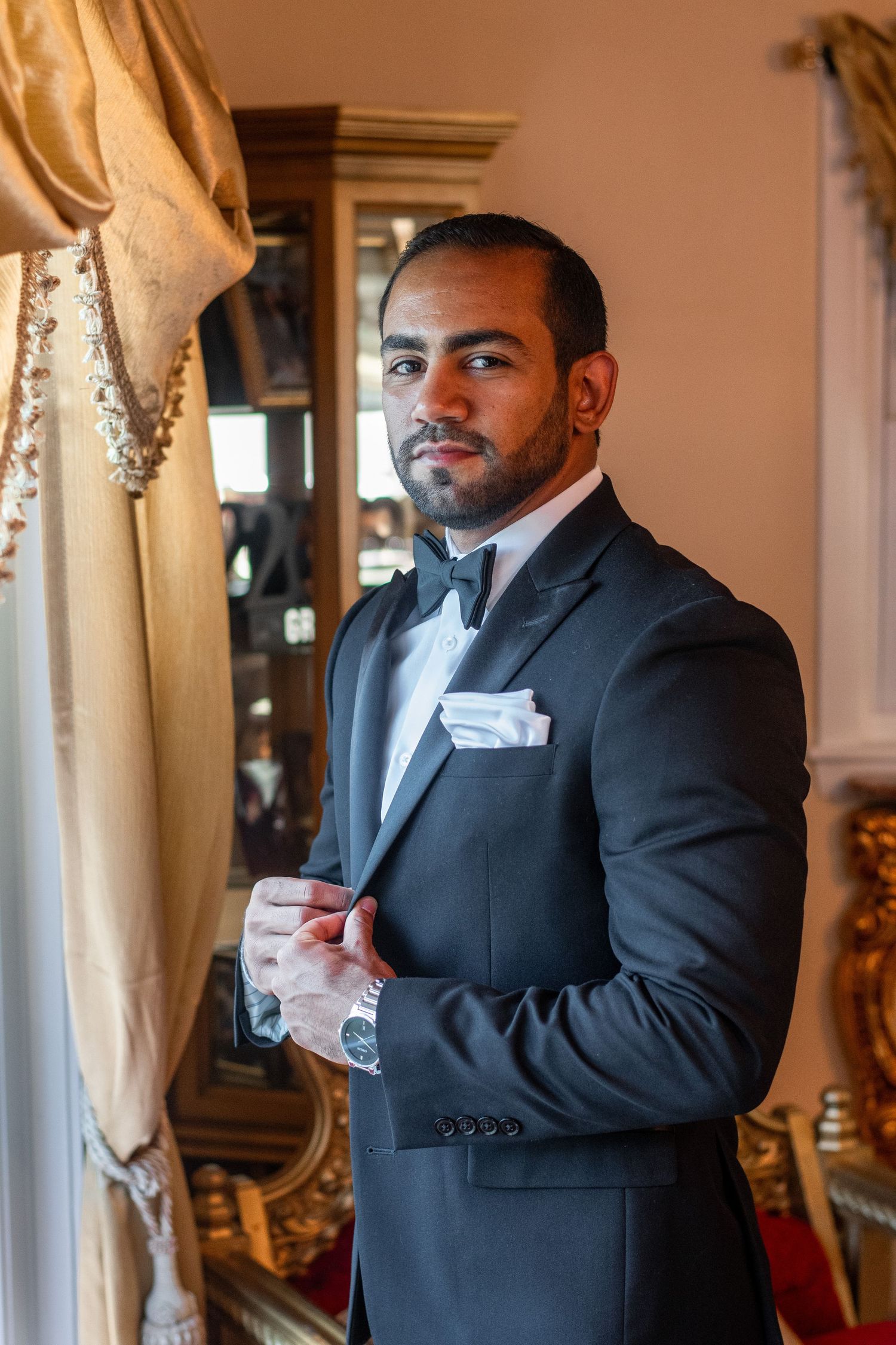 Sophisticated portrait of person in black tuxedo and bowtie against elegant interior.