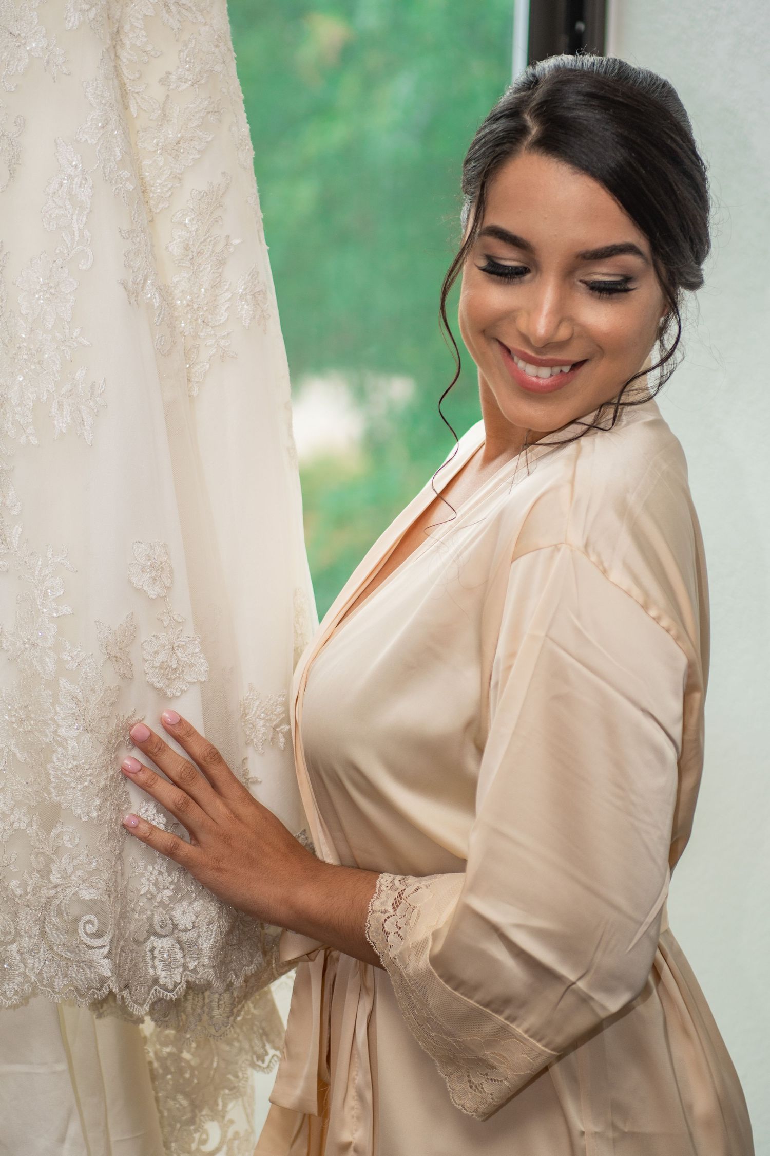 A bride in a silk robe admires her wedding dress during preparation.