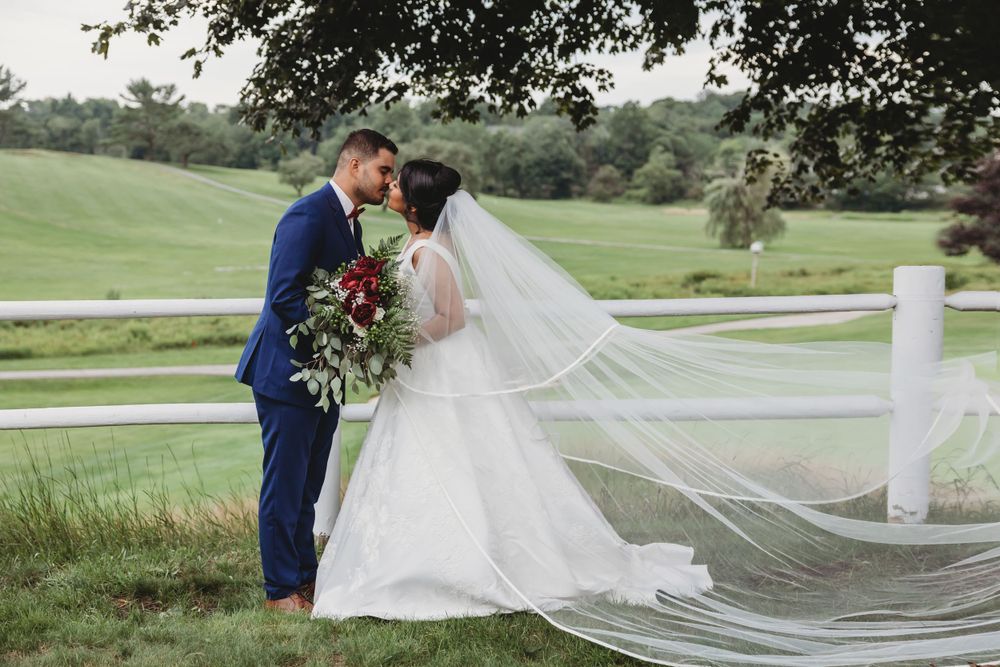 Bride and groom kissing outdoors on a green golf course, brides veil flowing in the wind behind her.