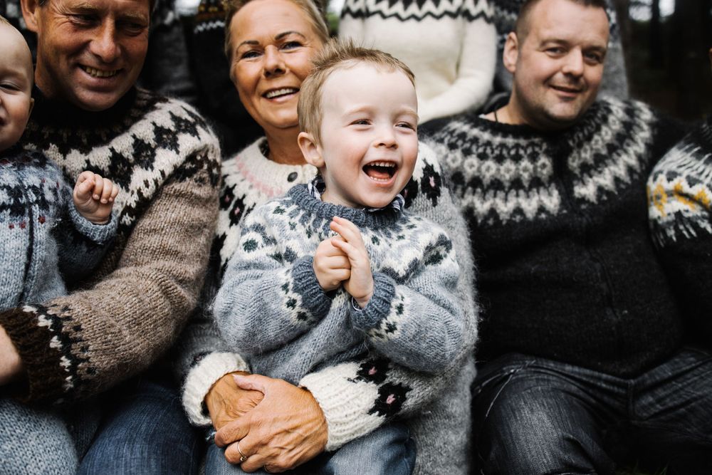 A joyful child laughs while surrounded by family members in matching patterned sweaters.