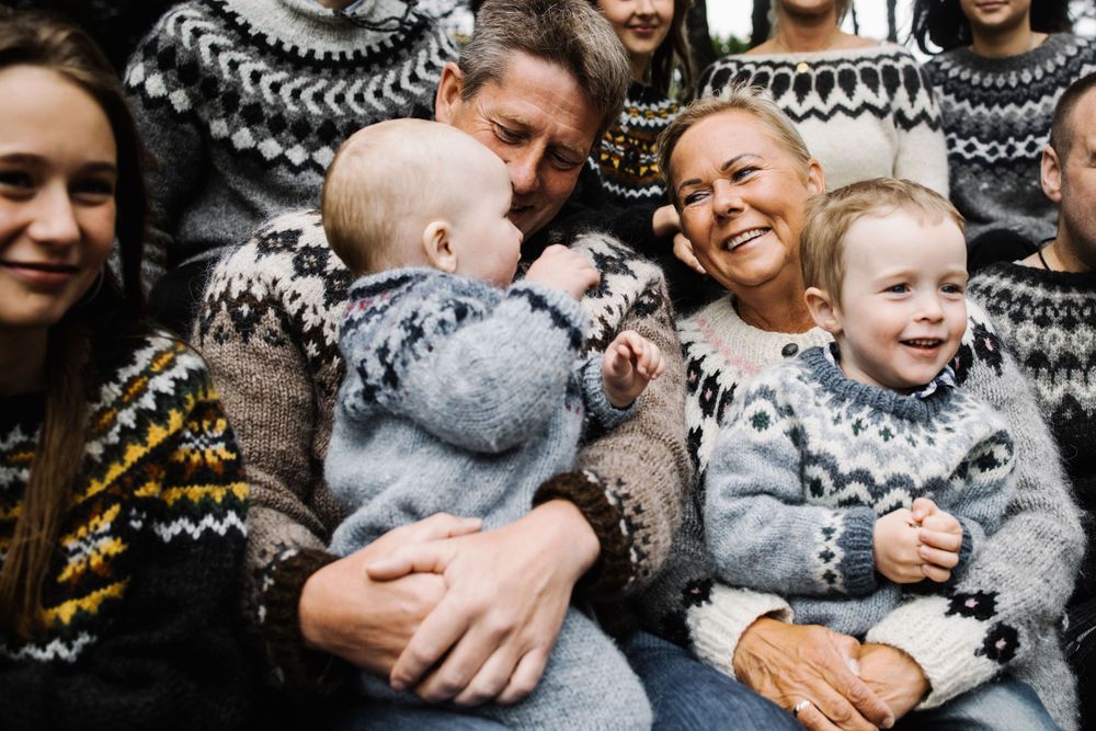 A cheerful family wearing matching Nordic sweaters share laughter while holding small children.