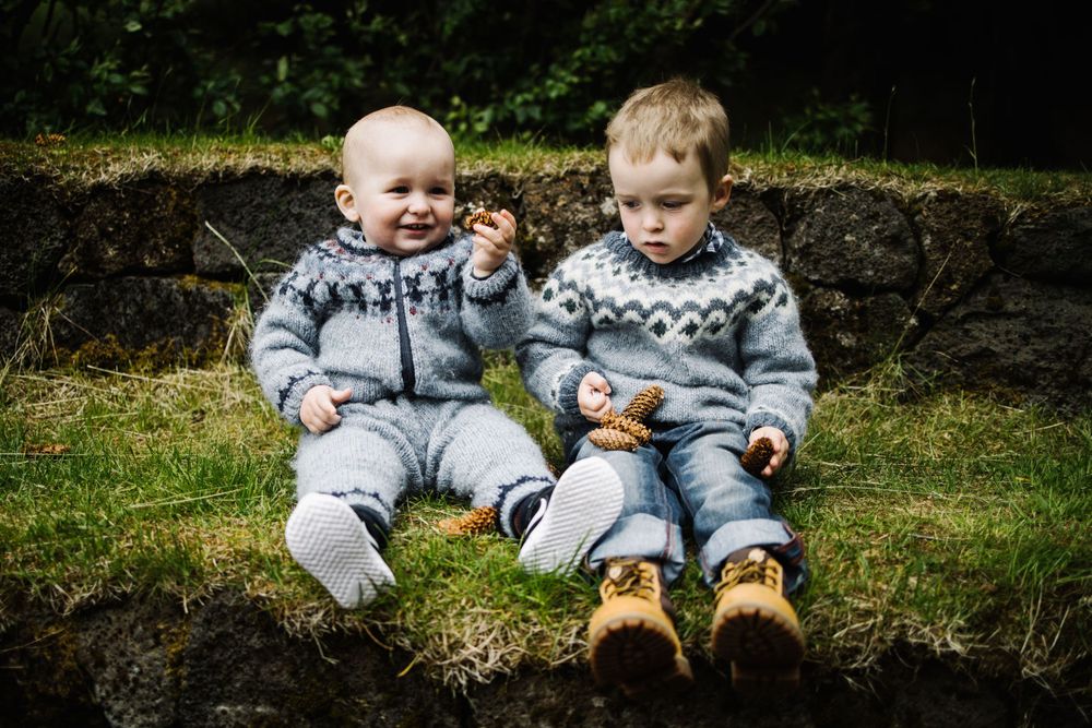 Two small children in matching gray patterned sweaters sitting on stone wall outdoors.