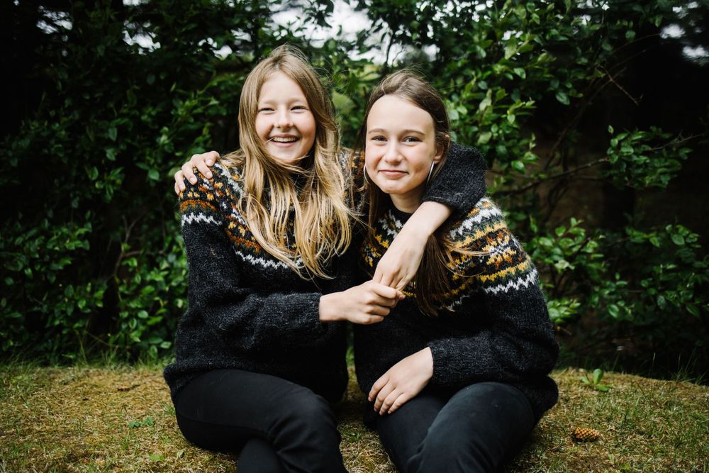 Two people wearing matching black fair isle sweaters embracing outdoors.