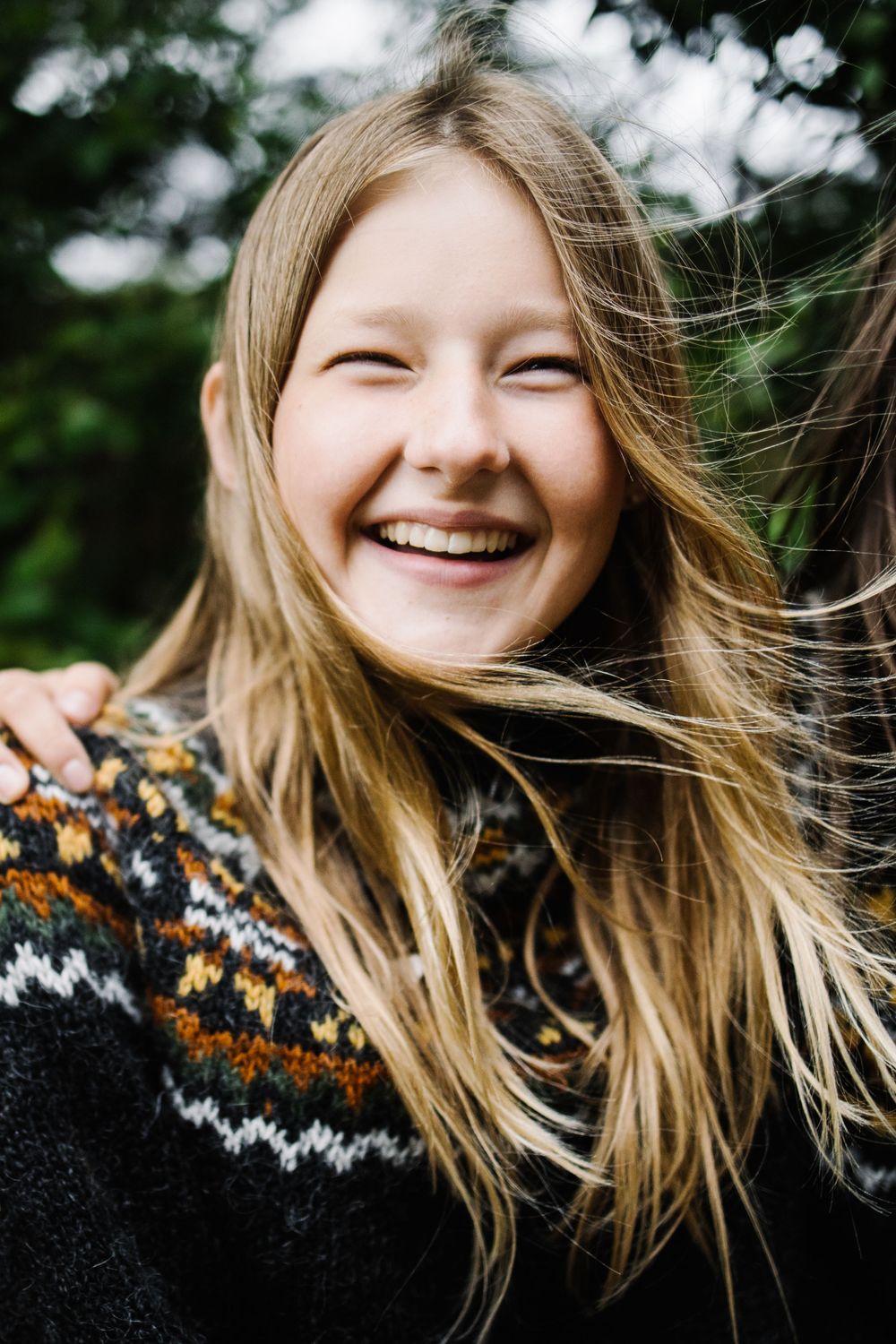 Person in black Nordic sweater with orange pattern smiling outdoors.