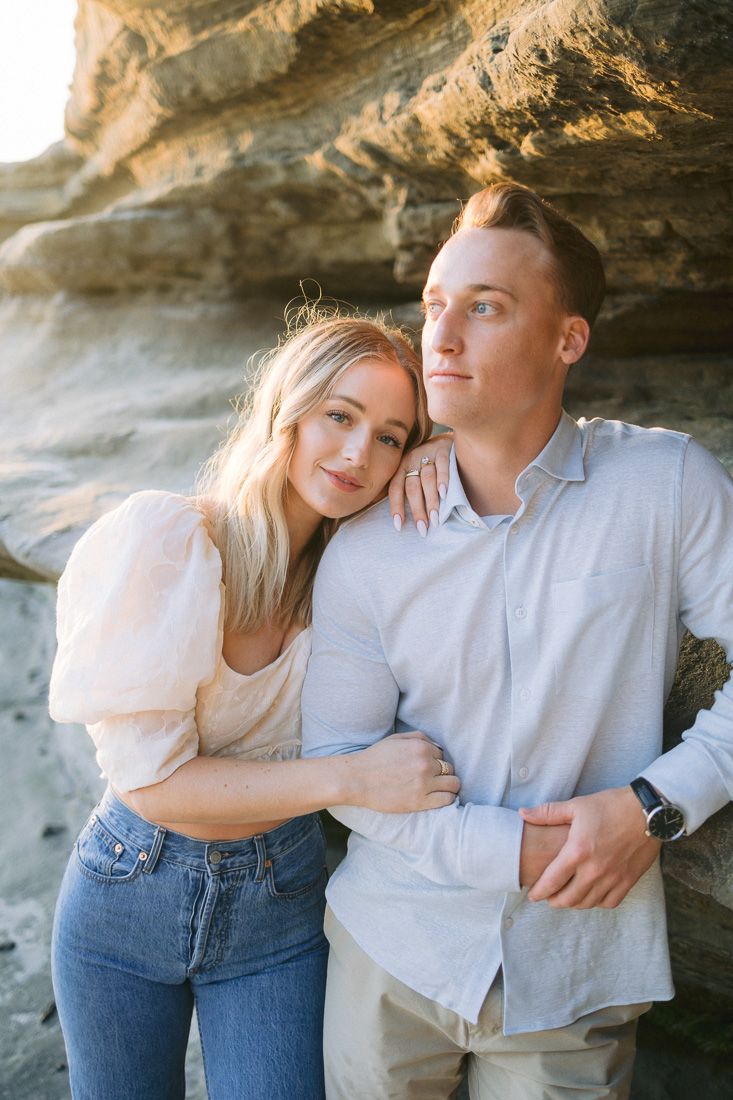 A couple poses together against rugged coastal cliffs during golden hour.