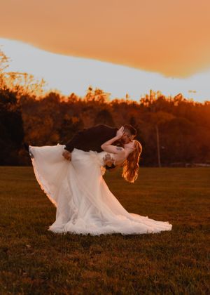 Bride's white wedding dress flows dramatically during sunset photos in an open field.