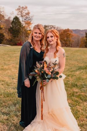 Wedding party members pose in dark attire and light gown against autumn landscape.
