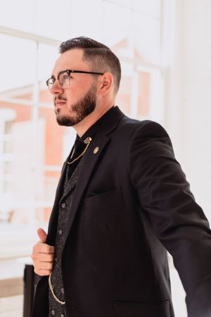Close-up profile view of groom in formal black suit and glasses.