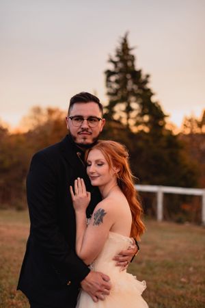 A romantic sunset wedding portrait in an outdoor field with warm autumn lighting.