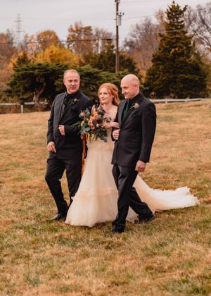 Wedding party members playfully pose in a grassy field during autumn sunset.