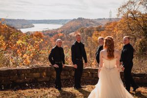 Wedding party gathered on a scenic overlook during autumn with colorful fall foliage in the background.