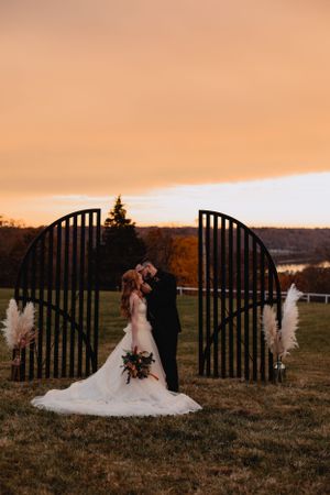 Wedding couple shares an intimate moment against a golden sunset with a rustic fence silhouette.