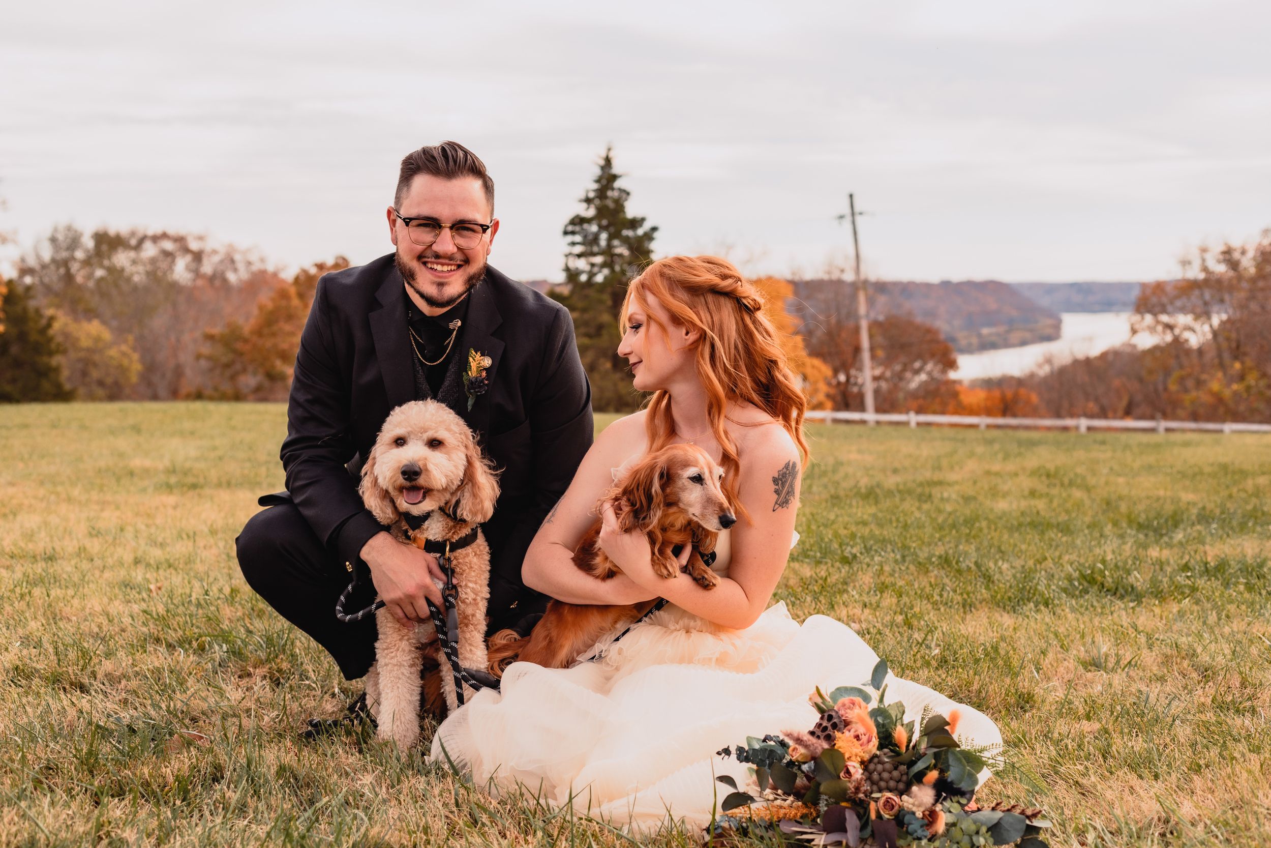 A couple takes wedding photos in a sunny field with their dog.